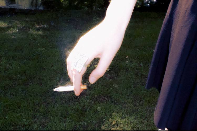 A hand with a ring holding a cigarette over grass